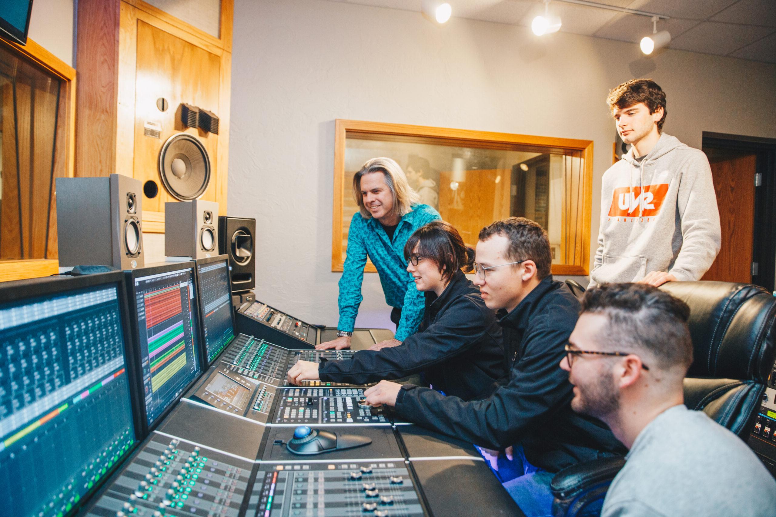 Students working together in the SNU recording studio while sitting in front of a control board